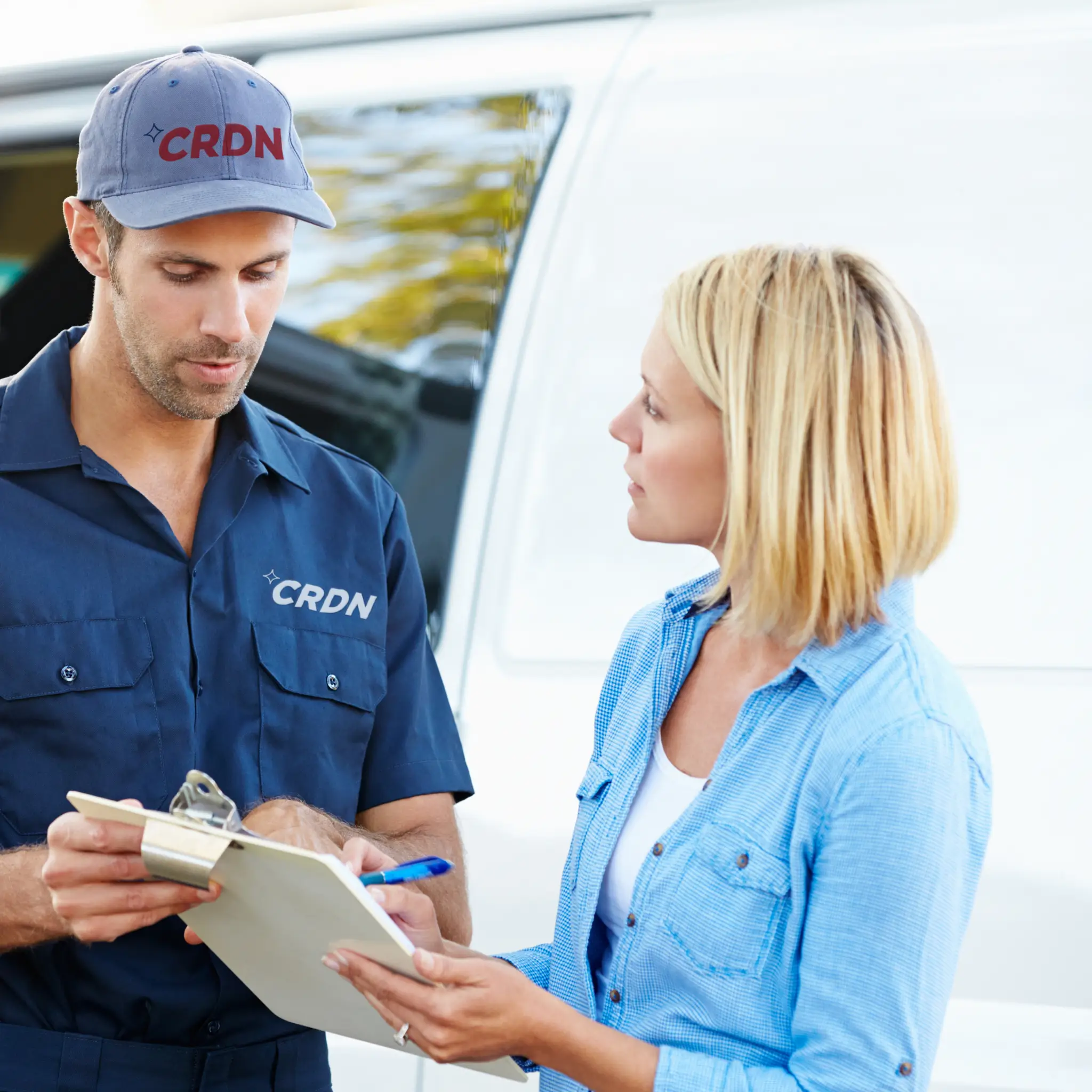 A CRDN technician discusses details with a client while holding a clipboard, near a service van in a sunny outdoor setting.